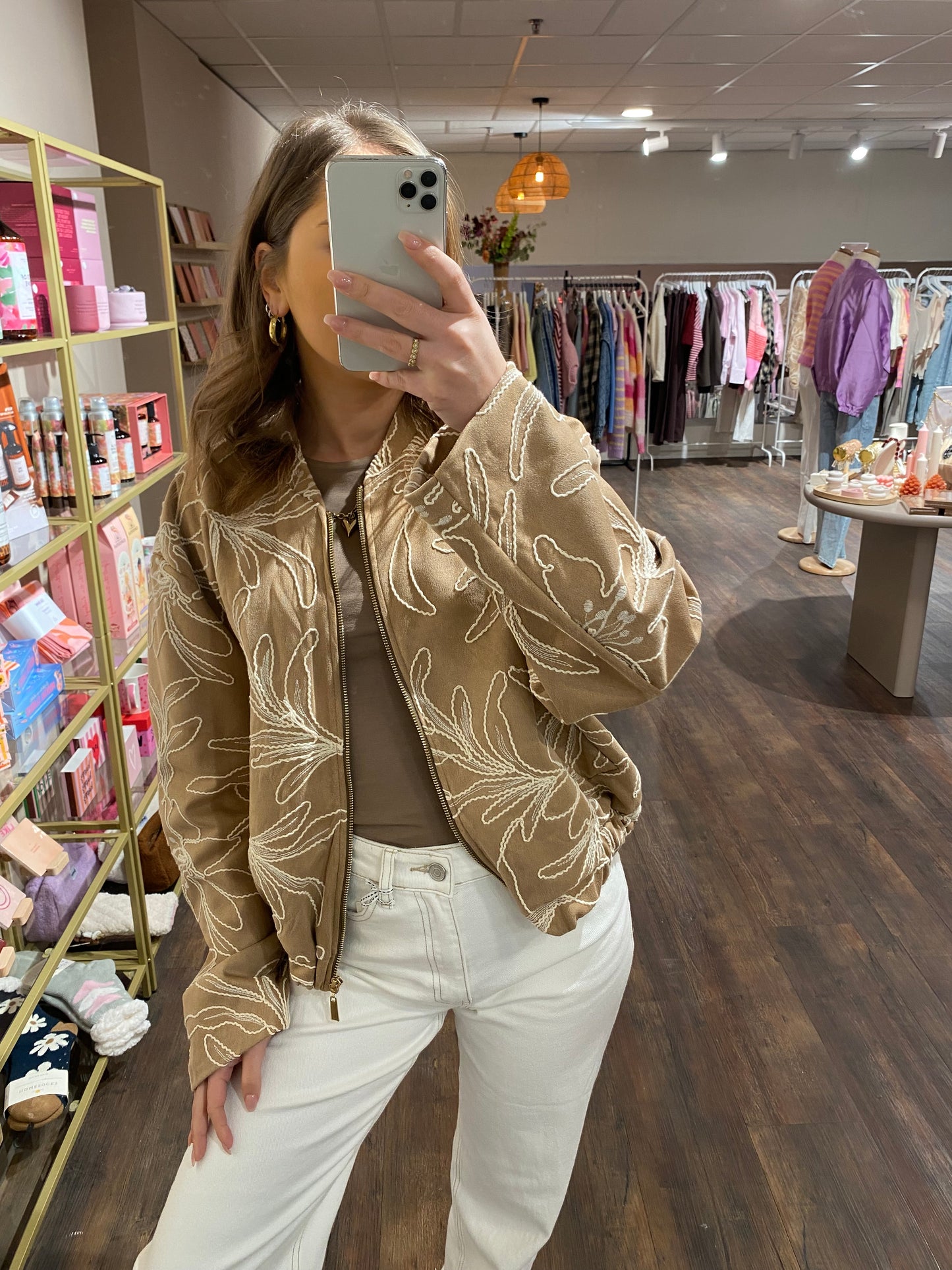 Beige bomberjasje met wit geborduurde bloemen.