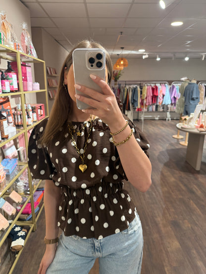 Bruine top met witte stippen en korte mouwen.