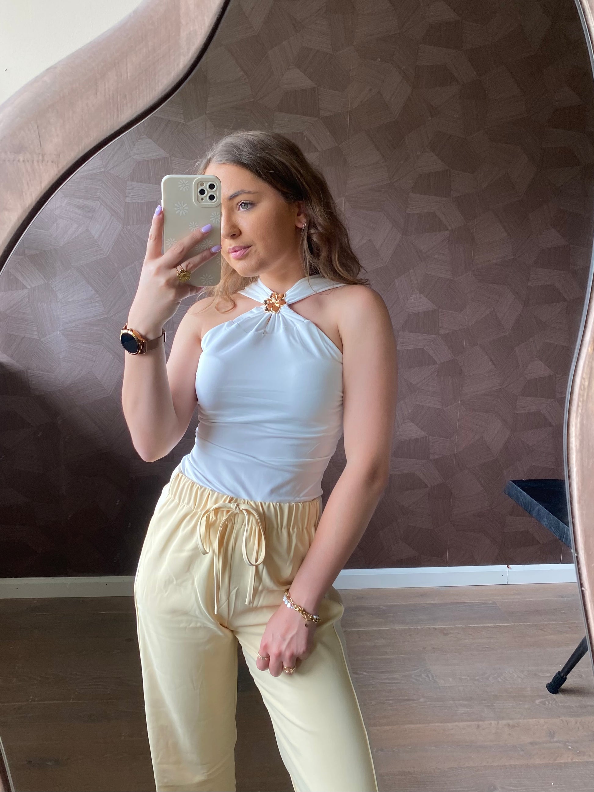 Model draagt witte halter top met gouden bloem voorop