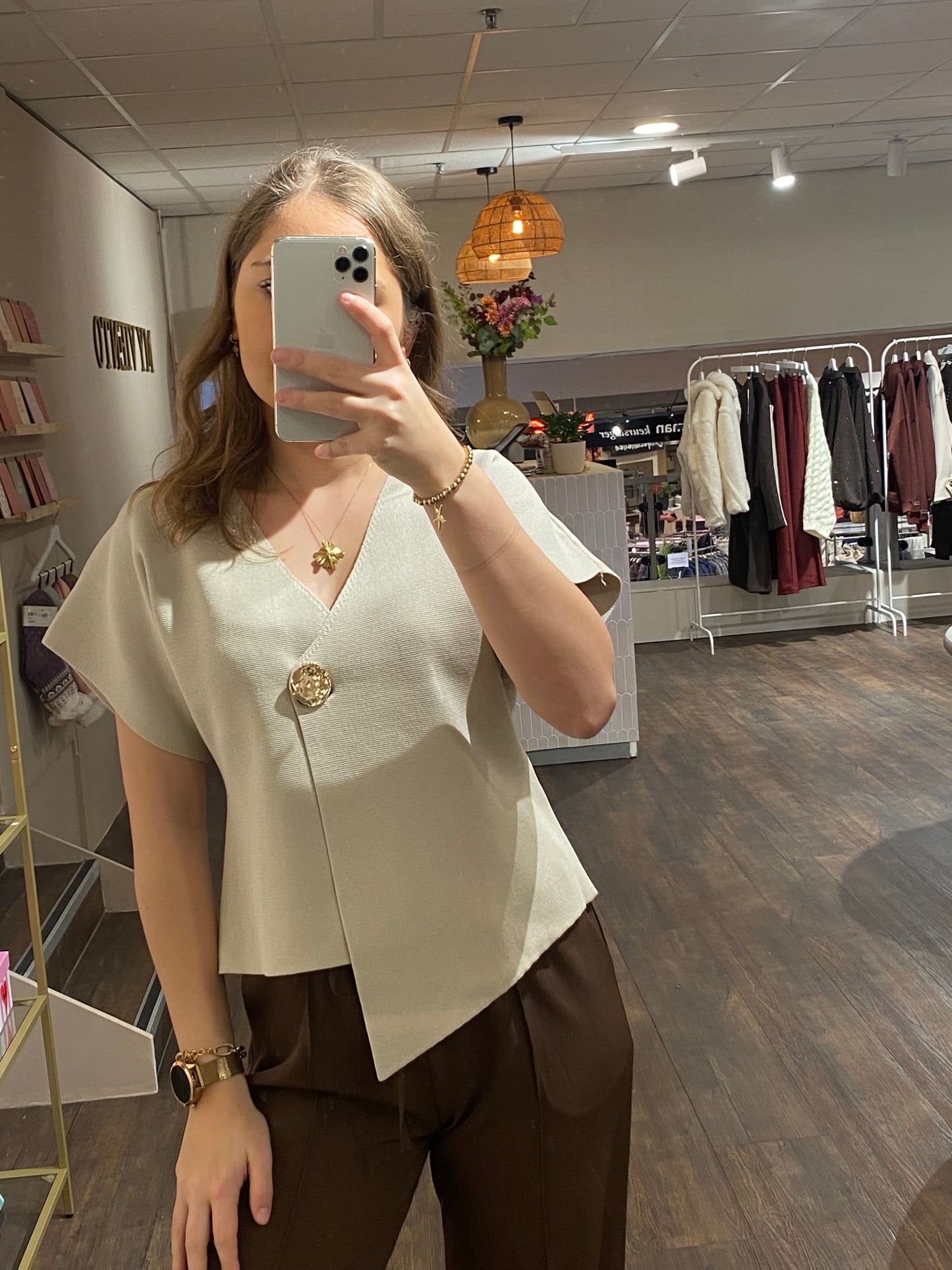Beige asymmetrische top met V-hals en opvallende gouden knop als detail.