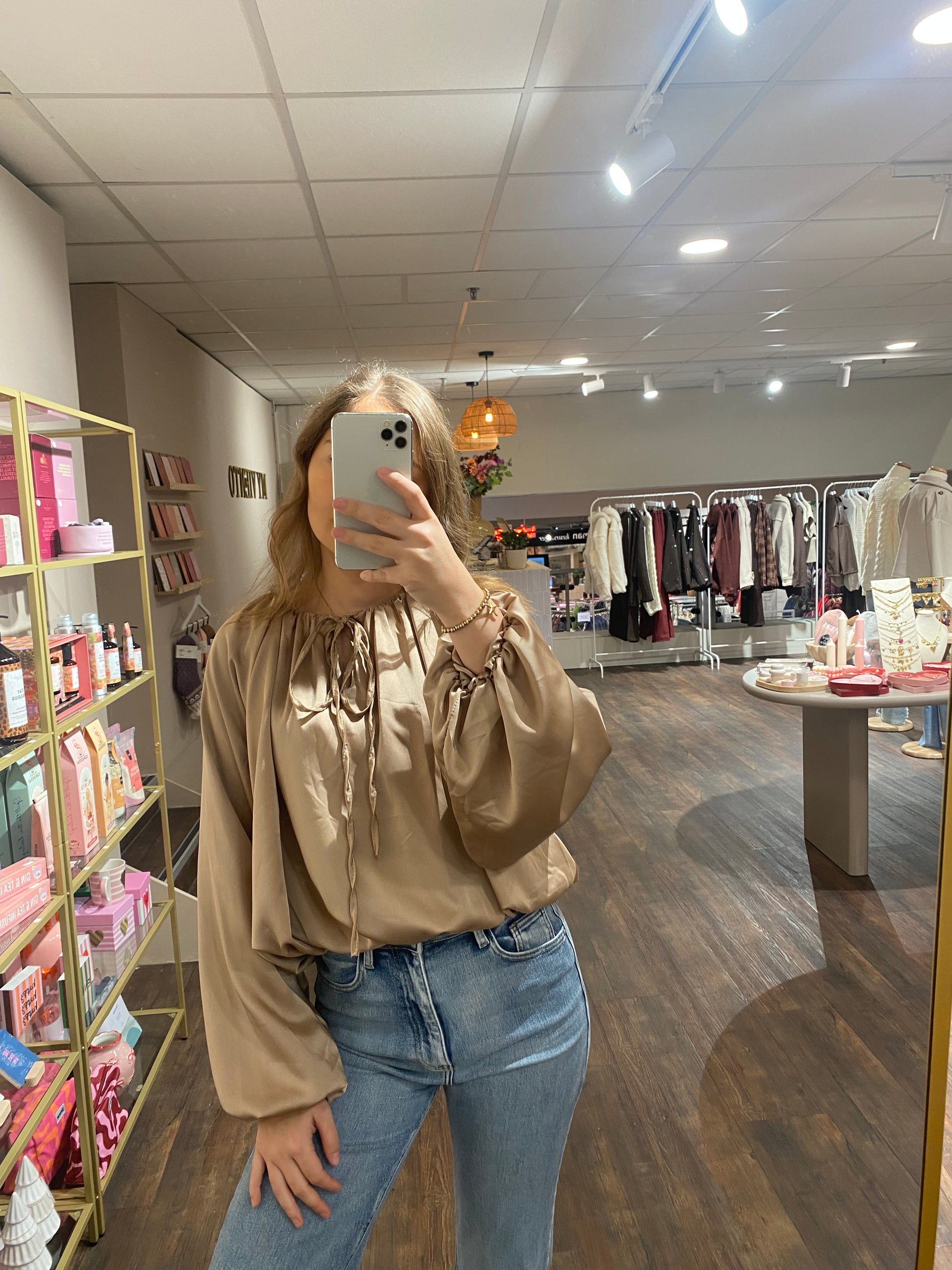 Beige satijnachtige blouse met pofmouwen en touwtjes bij de hals.