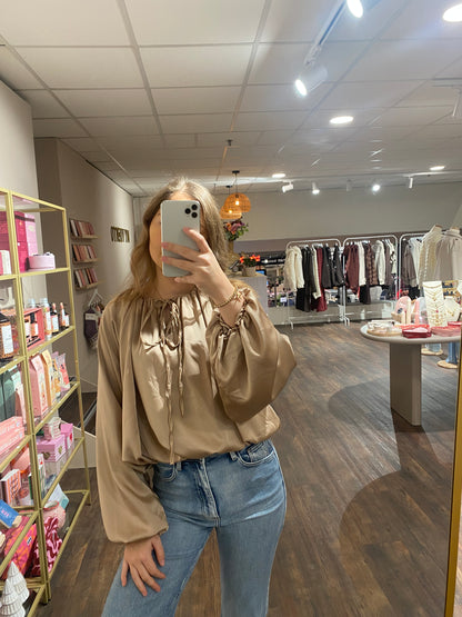 Beige satijnachtige blouse met pofmouwen en touwtjes bij de hals.